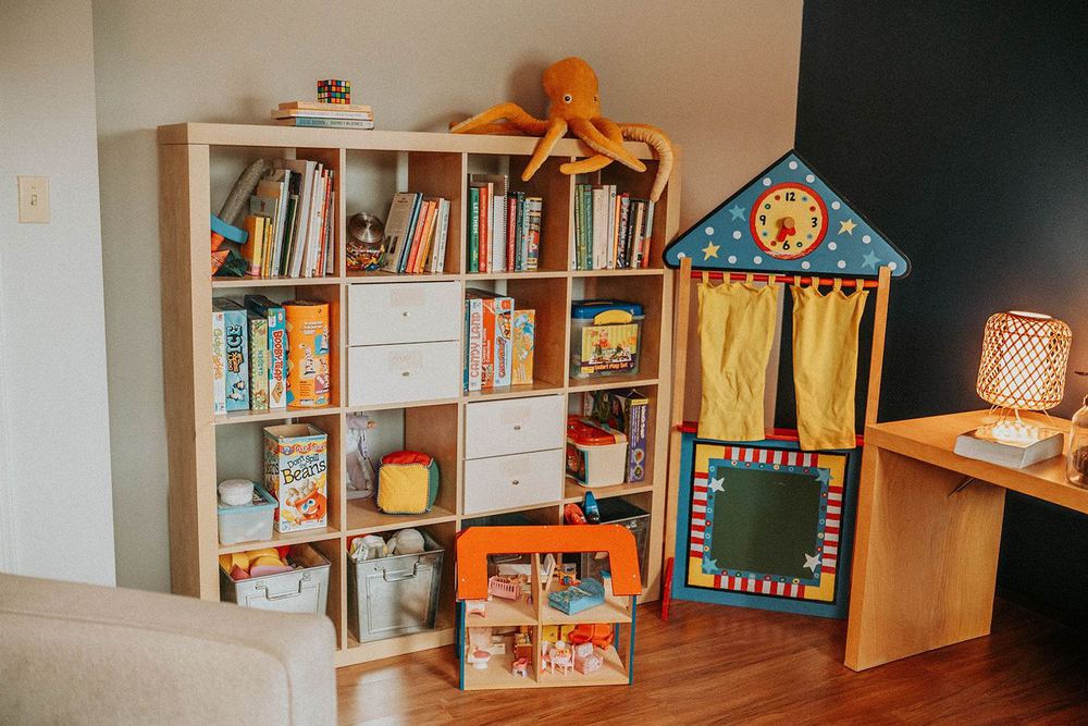 A corner of the Willow Tree playroom: a bookshelf packed with games and books, a fabric puppet theatre with a chalkboard, and a large stuffed octopus on top.