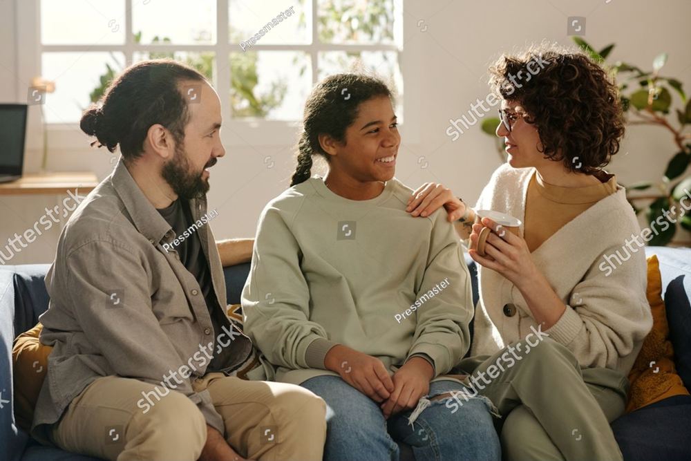 Two parents and their teenage daughter sitting close together on a sofa, talking.