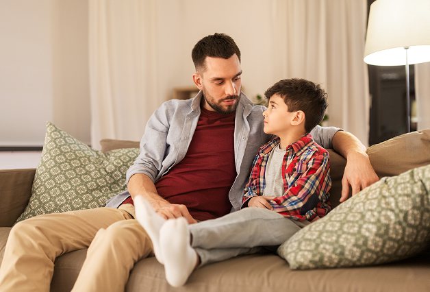A parent and child sitting together on a sofa, talking.